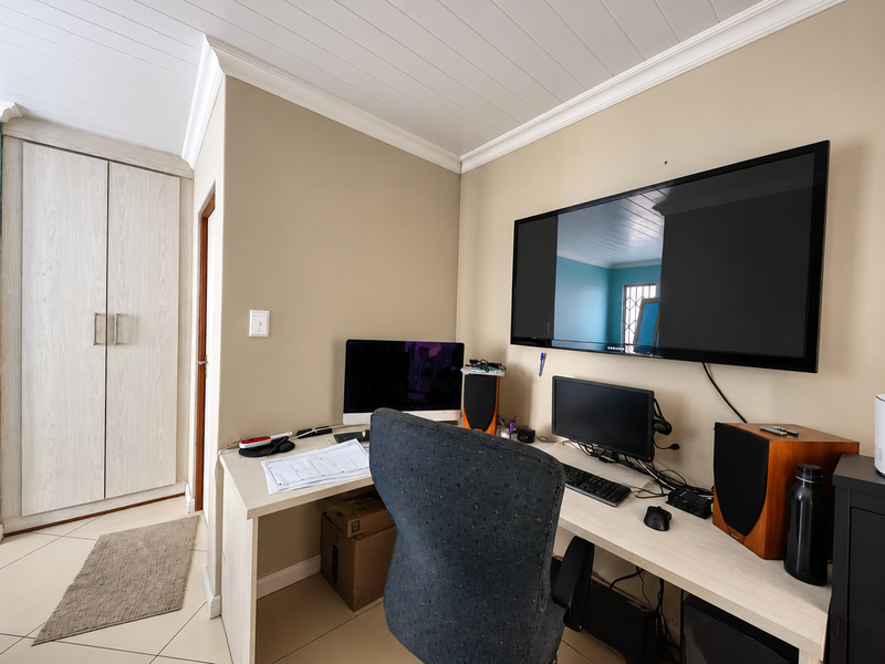 A functional home office featuring built-in wardrobe storage, tiled flooring, and a classic tongue and groove ceiling with crown molding.