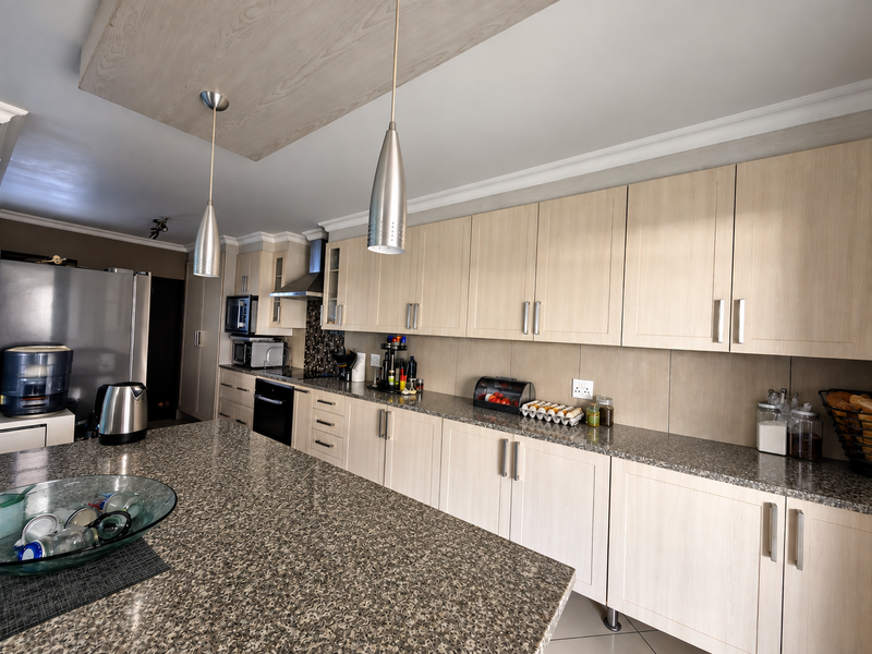 Modern kitchen featuring light wood cabinetry, granite countertops, integrated oven, extractor fan, and stylish pendant lighting over a spacious island.
