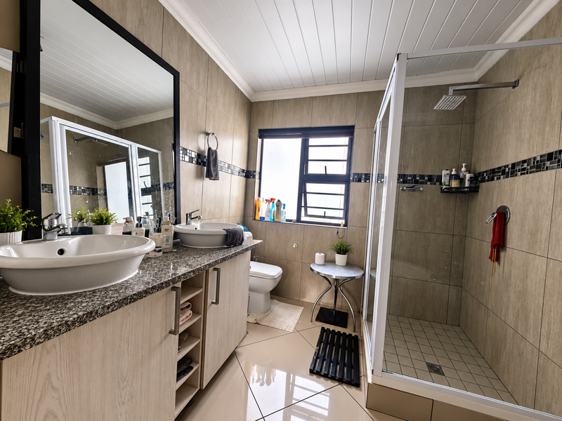 Modern bathroom featuring a dual vanity with granite countertops, vessel sinks, a large mirror, and a spacious glass-enclosed shower with a rain shower head.