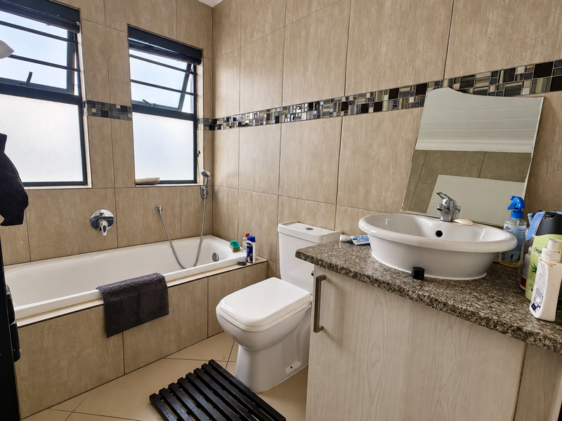 A functional bathroom featuring a built-in bathtub with handheld shower, a vessel sink on a granite vanity, and neutral wall tiling with mosaic accents.