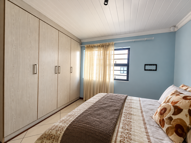 A well-maintained bedroom featuring extensive built-in cupboards, light-toned tiled flooring, and a classic tongue and groove ceiling finish.