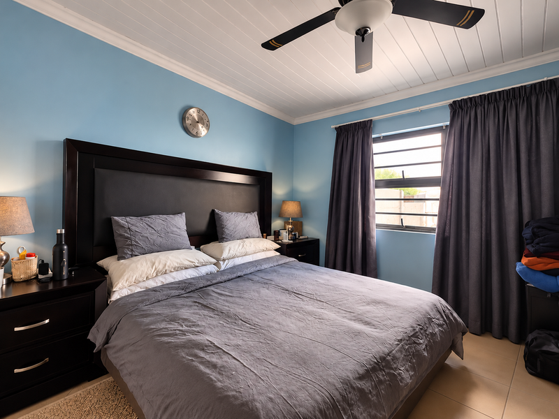 A well-maintained bedroom featuring a tongue and groove ceiling with a fan, tiled flooring, and large windows with dark curtains.
