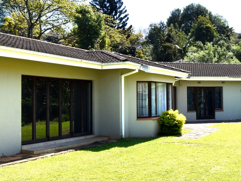 Rear view of the house featuring a tiled roof, large sliding glass doors, a bay window, and a paved walkway leading to the garden.