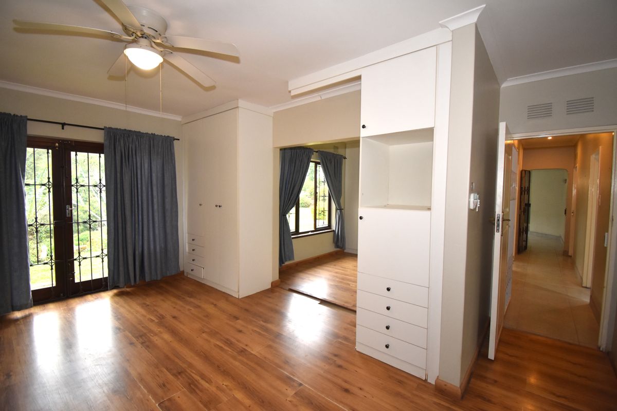 Spacious bedroom featuring laminate flooring, built-in cupboards, a ceiling fan, and direct access to the garden through a secure sliding door.