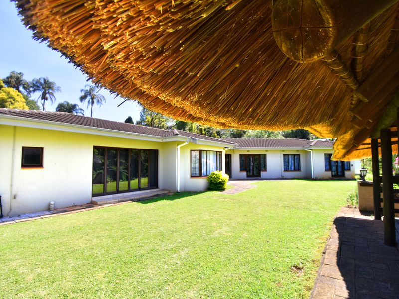 A view of the rear garden featuring a well-maintained lawn, paved pathways, and a large thatched-roof patio area overlooking the house exterior.
