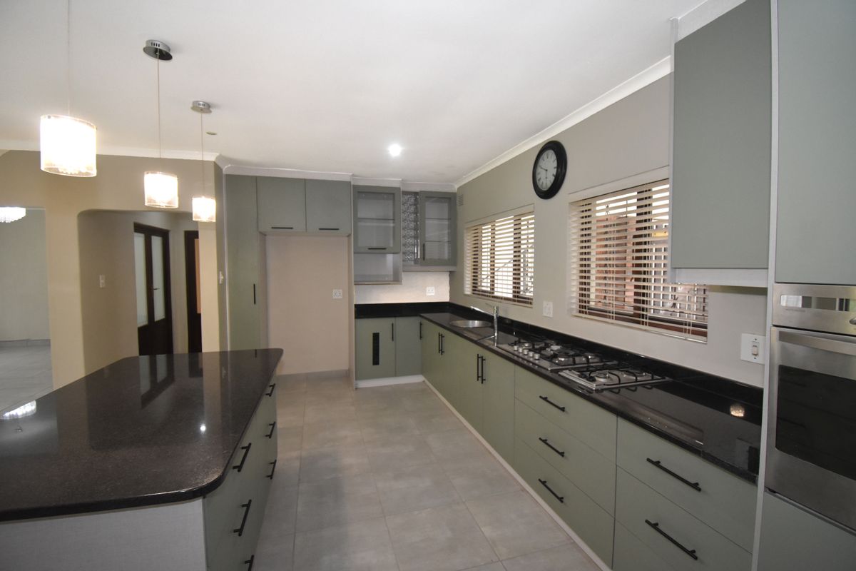 Modern kitchen featuring sage green cabinetry, dark granite countertops, a central island, built-in oven, and gas hob with tiled flooring throughout.