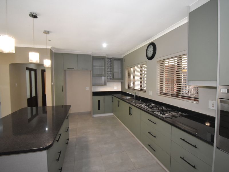 Modern kitchen featuring sage green cabinetry, dark granite countertops, a central island, built-in oven, and gas hob with tiled flooring throughout.