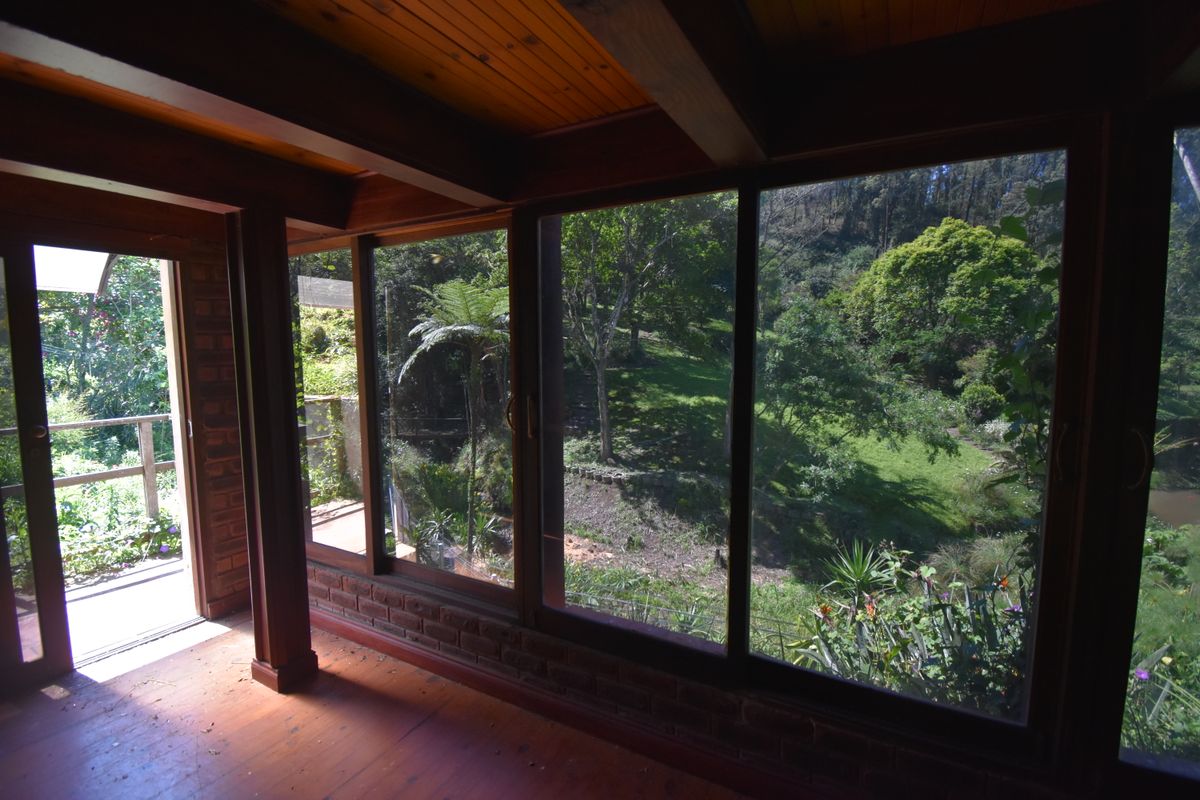 Sunlit living area featuring exposed timber beams, wood flooring, and expansive glass doors offering scenic views of the surrounding garden and landscape.