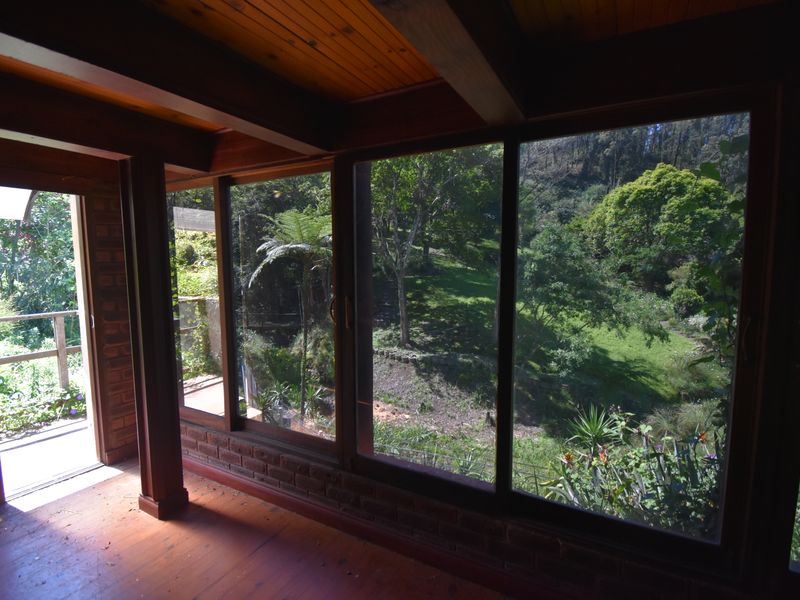 Sunlit living area featuring exposed timber beams, wood flooring, and expansive glass doors offering scenic views of the surrounding garden and landscape.