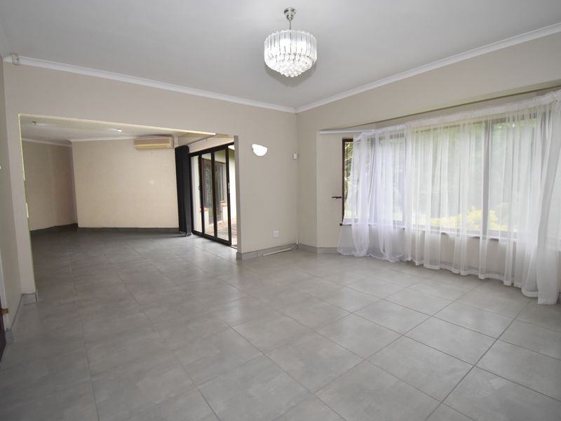 Spacious, light-filled living area featuring neutral tiled flooring, a large bay window, and direct access to an outdoor patio through sliding glass doors.