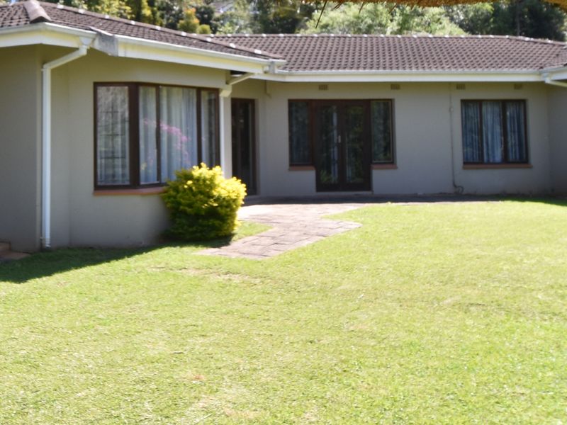Rear view of the house featuring a tiled roof, bay window, and french doors opening onto a paved walkway and garden area.