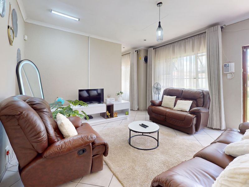 A bright living room featuring tiled flooring, neutral walls, and a large sliding glass door providing direct access to the garden area.