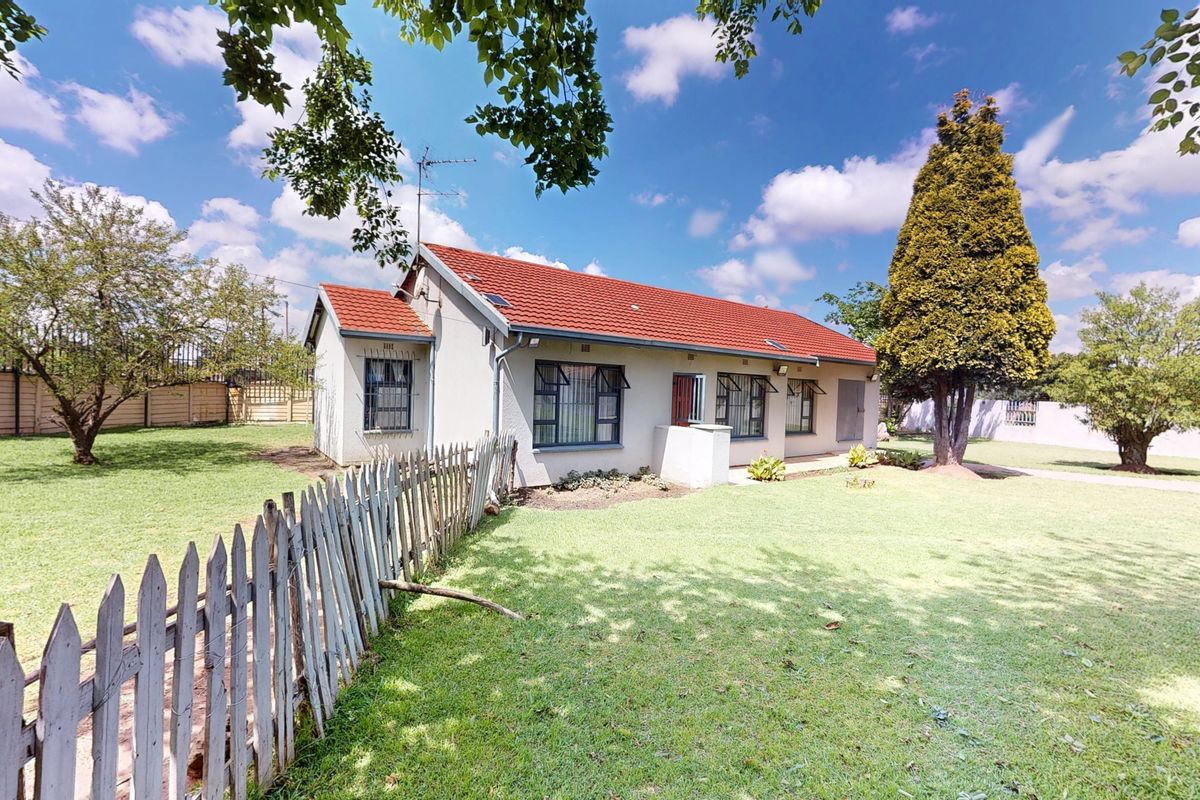 A view of the rear elevation of the house featuring a tiled roof, burglar bars on windows, and a spacious garden with a picket fence.