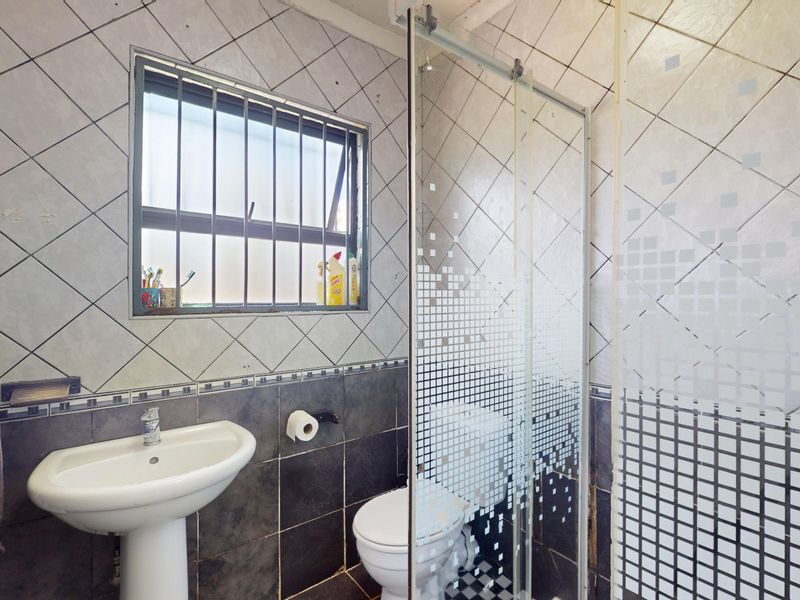 A dated bathroom featuring a pedestal basin, toilet, and shower enclosure with patterned glass, finished with tiled walls and floors.
