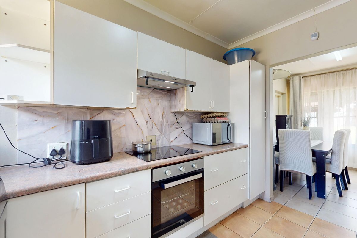 Functional kitchen featuring white cabinetry, marble-effect splashback, built-in oven, and electric hob, with direct access to the adjacent dining area.