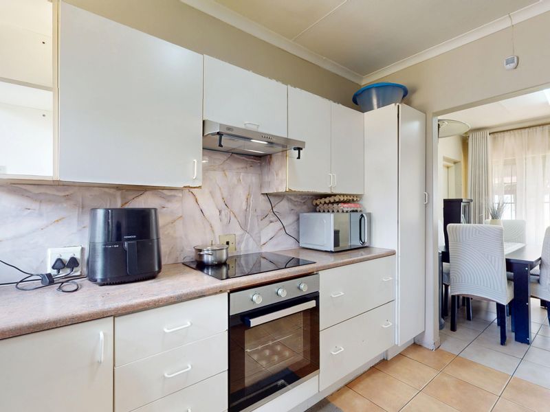 Functional kitchen featuring white cabinetry, marble-effect splashback, built-in oven, and electric hob, with direct access to the adjacent dining area.