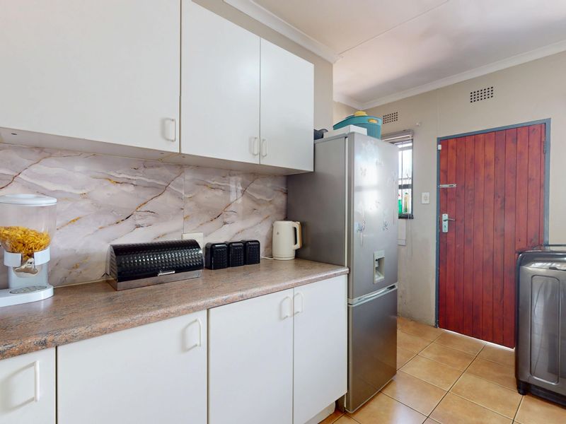 Functional laundry area featuring built-in cabinetry, laminate countertops, marble-effect splashback, and tiled flooring with direct exterior access.
