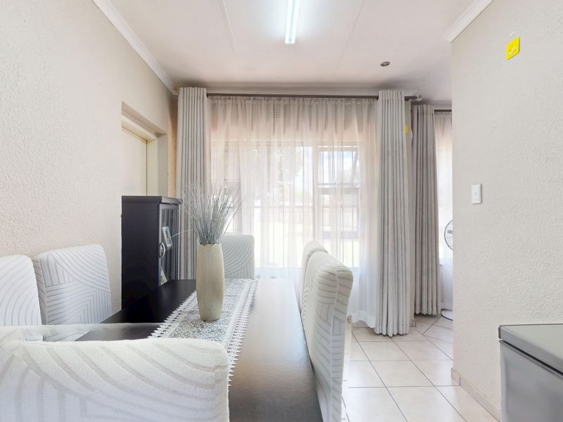 A bright dining area featuring neutral tiled flooring and large windows with curtain tracks, offering a clean and functional space for family meals.