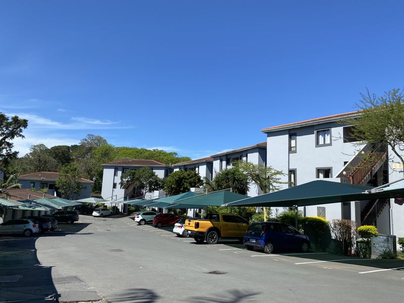 Exterior view of an apartment complex featuring paved parking areas with shade cloth carports and multi-story residential buildings.