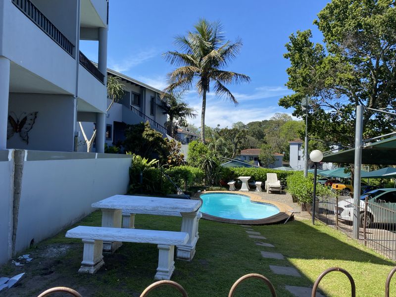 Communal outdoor area featuring a swimming pool, landscaped garden, and paved seating space, set within a multi-story apartment complex.
