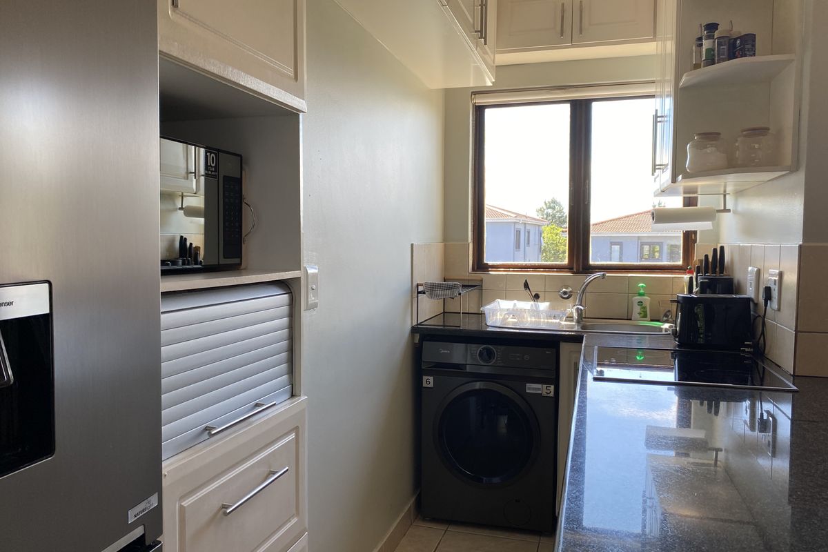 A compact, well-maintained kitchen featuring granite countertops, ample built-in cabinetry, an integrated microwave, and a functional layout with a window for natural light.