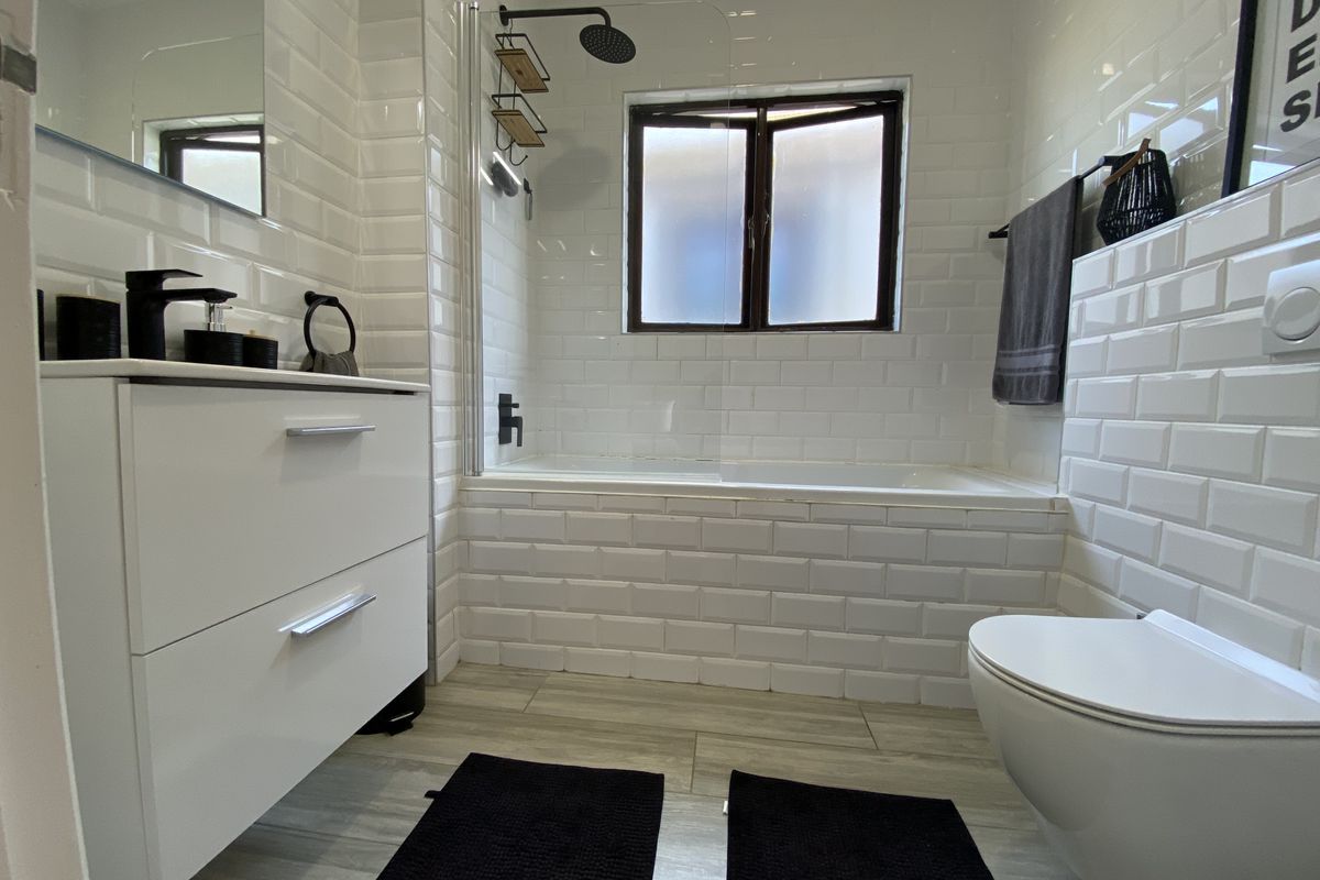 Modern bathroom featuring a wall-mounted toilet, vanity cabinet, and a bathtub with shower fixtures, finished with clean white subway tiles.