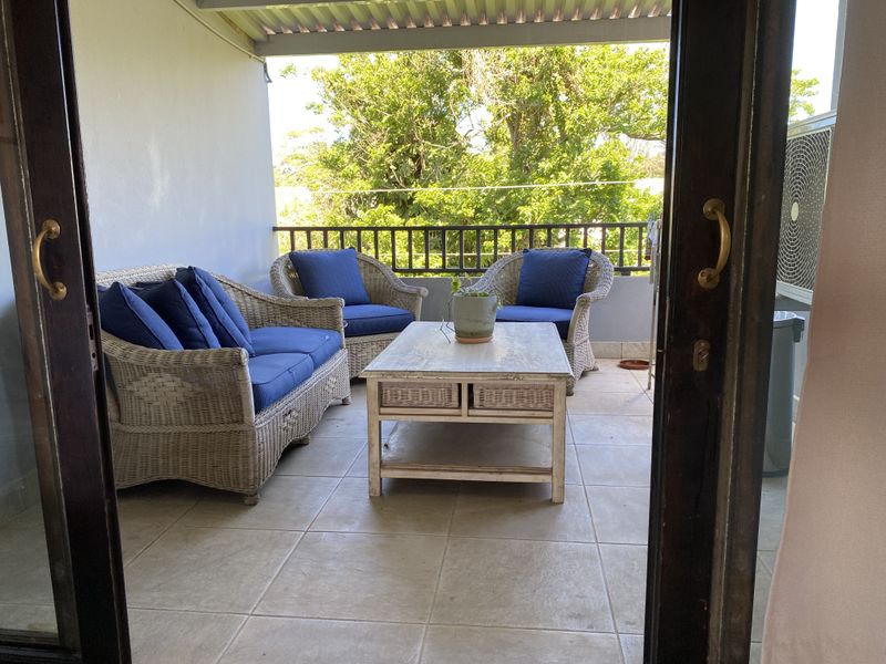 A covered balcony featuring tiled flooring and a metal balustrade, providing a pleasant outdoor space accessible through sliding doors.