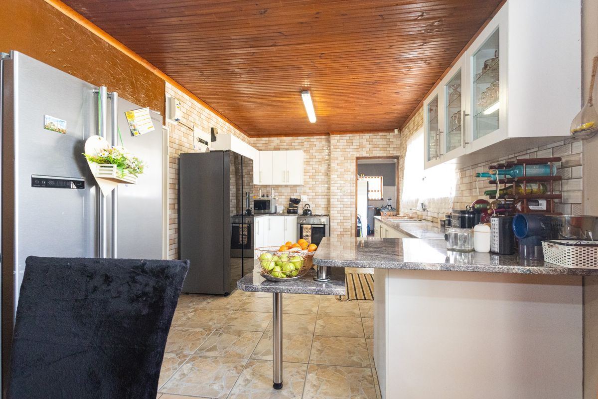 A functional kitchen featuring granite countertops, ample built-in cabinetry, tiled flooring, and a distinctive timber-paneled ceiling with a breakfast bar area.