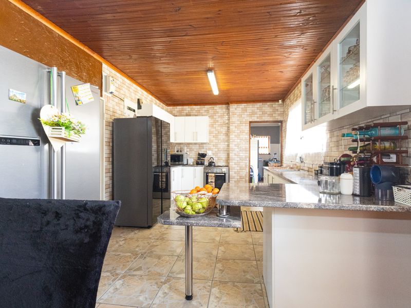 A functional kitchen featuring granite countertops, ample built-in cabinetry, tiled flooring, and a distinctive timber-paneled ceiling with a breakfast bar area.