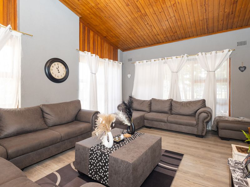 Spacious living room featuring a high timber-clad vaulted ceiling, light laminate flooring, and large windows that provide ample natural light.