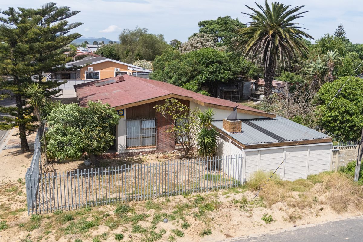 Aerial view of a detached house featuring a metal roof, brick facade, and secure perimeter fencing, set on a large plot with established trees.