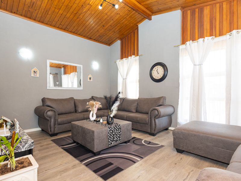 Spacious living room featuring a high vaulted timber ceiling, laminate flooring, and warm timber wall accents, creating a cozy and inviting atmosphere.