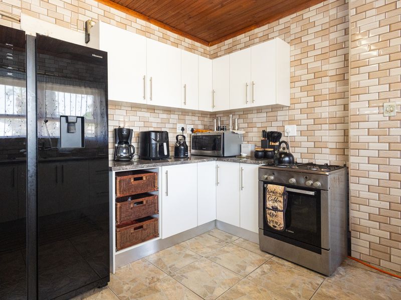 A functional kitchen featuring white cabinetry, a gas stove with oven, tiled backsplash, and a timber ceiling, offering a practical layout for daily cooking.