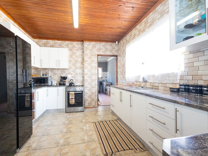 A functional kitchen featuring white cabinetry, stone countertops, a stainless steel oven, and a distinctive timber-paneled ceiling with tiled walls and flooring.