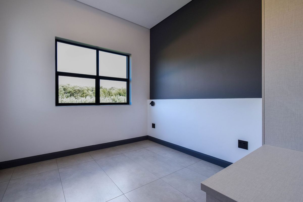 A bright, modern bedroom featuring neutral tiled flooring, a striking two-tone feature wall, and a large window with black framing.