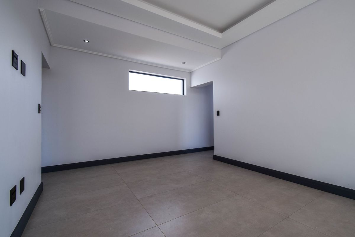 A bright, modern, and empty room featuring neutral tiled flooring, recessed ceiling lighting, and contrasting dark skirting boards.