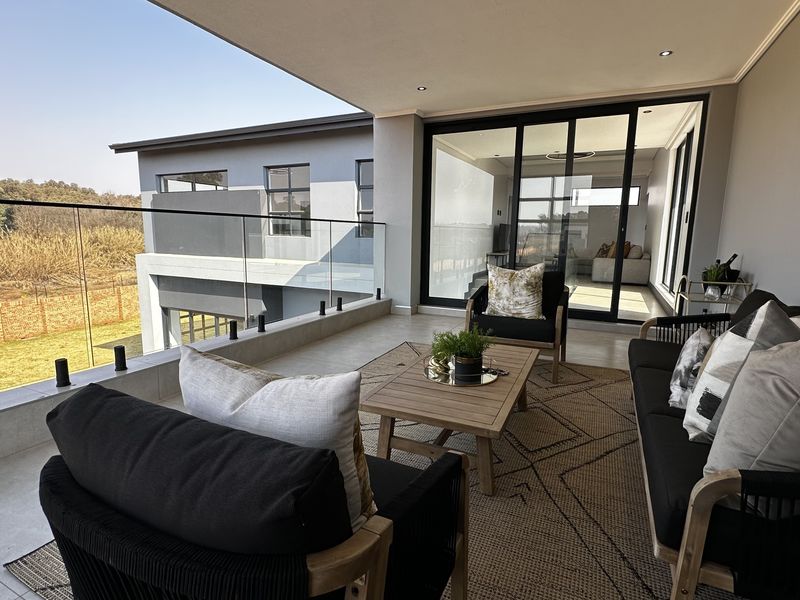 Spacious covered balcony featuring modern tiled flooring, a sleek glass balustrade, and seamless access to the interior living area through large sliding doors.