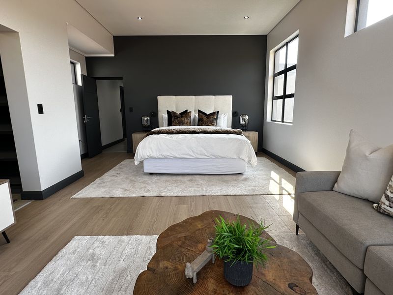 Spacious modern bedroom featuring laminate flooring, a dark accent wall, recessed lighting, and an integrated walk-in closet area.