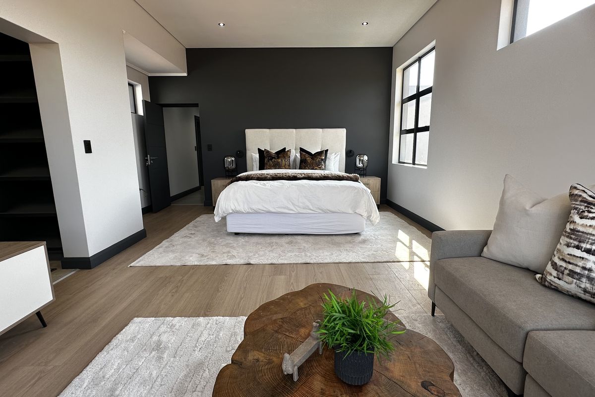 Spacious modern bedroom featuring laminate flooring, a dark accent wall, recessed lighting, and an integrated walk-in closet area.