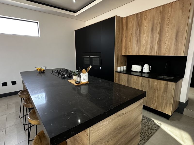 Modern kitchen featuring a large central island with a gas hob, sleek wood-grain cabinetry, black stone countertops, and integrated built-in ovens.