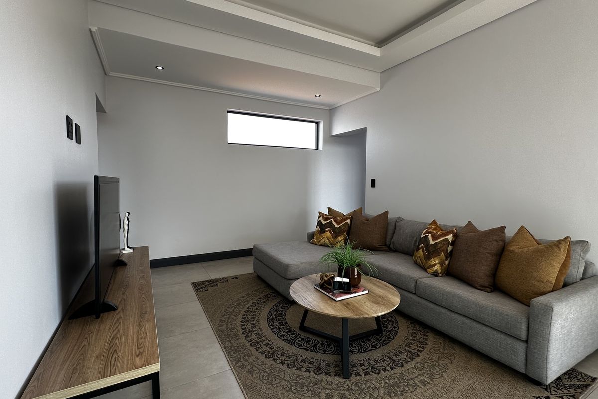 A modern living room featuring a recessed ceiling with integrated downlights and neutral tiled flooring.