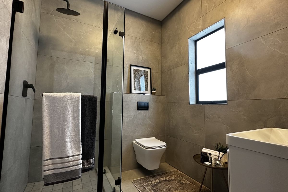 Modern bathroom featuring large format grey tiles, a walk-in shower with black fixtures, and a wall-mounted toilet.