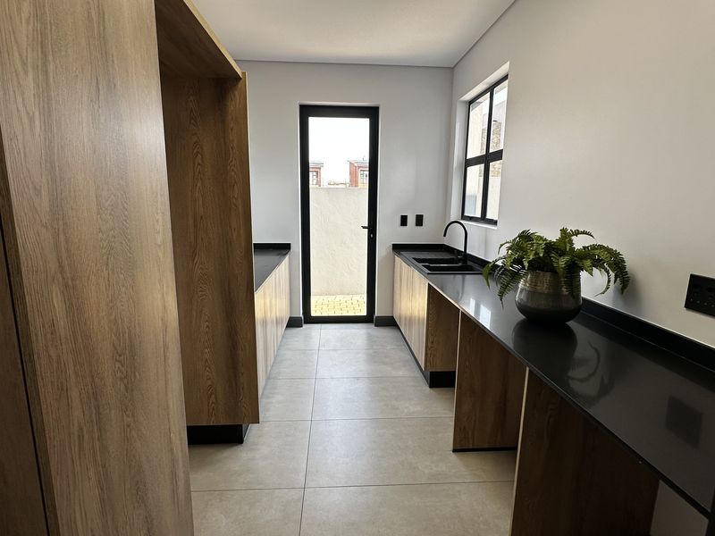 Modern scullery featuring wood-grain cabinetry, sleek black countertops, an undermount sink, and direct access to an outdoor area.