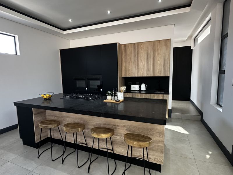 Modern kitchen featuring a large central island with stone countertops, integrated gas hob, built-in ovens, and high-quality wood and matte black cabinetry.
