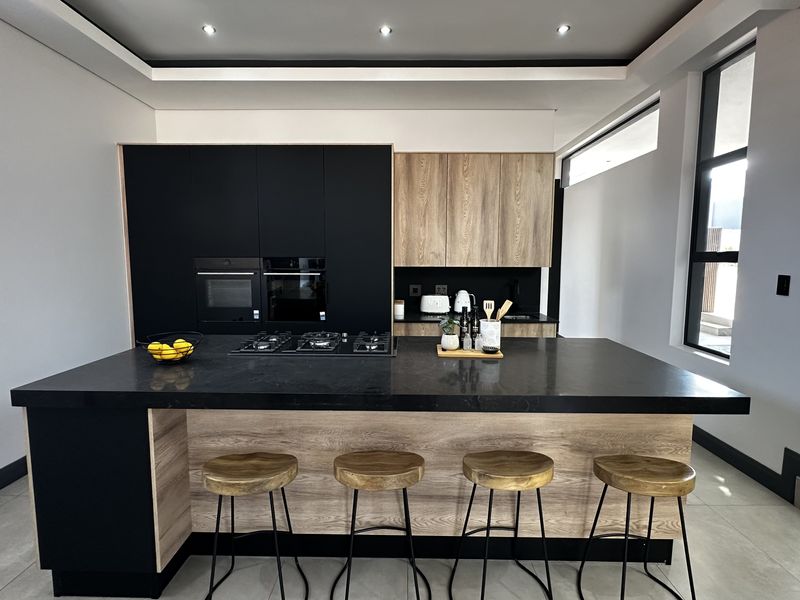 Modern kitchen featuring a large central island with stone countertops, built-in oven, gas hob, and a sleek combination of black and wood-grain cabinetry.