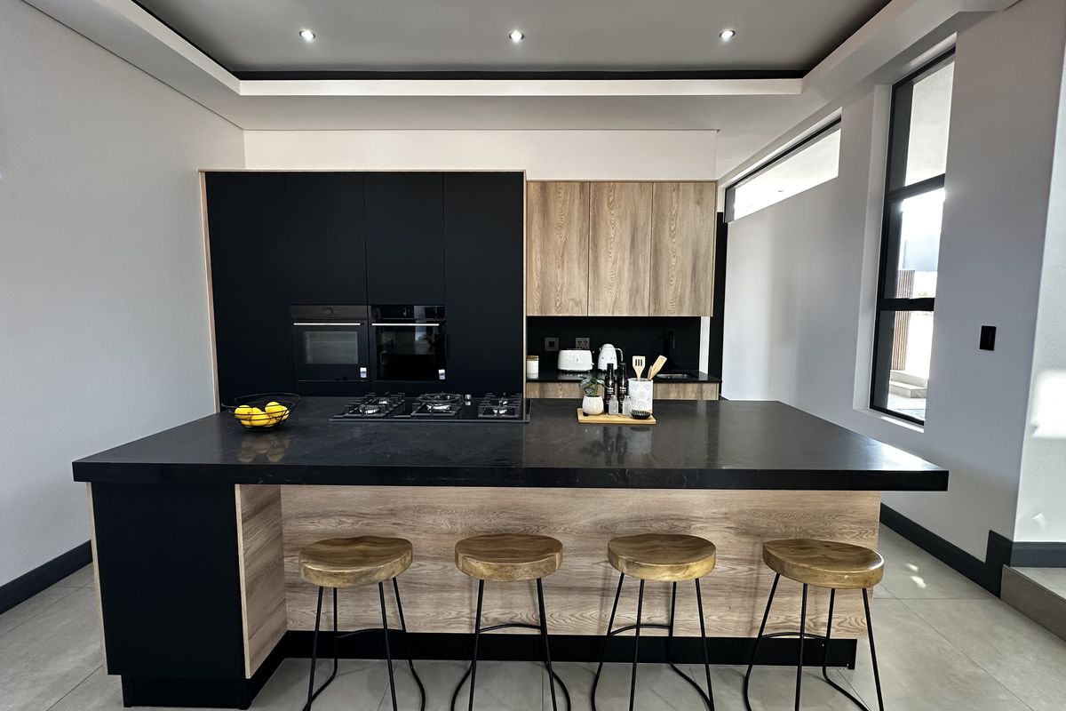 Modern kitchen featuring a large central island with stone countertops, built-in oven, gas hob, and a sleek combination of black and wood-grain cabinetry.