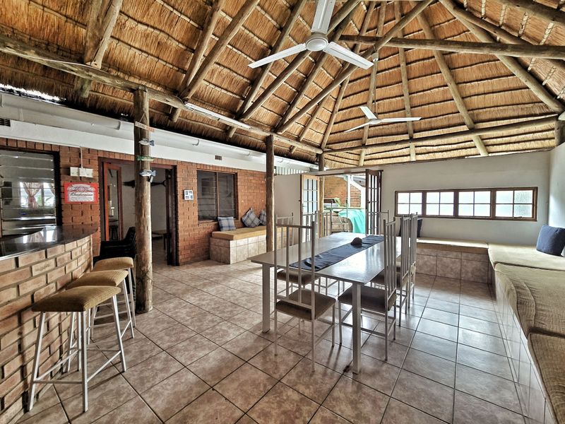 Spacious covered patio featuring a rustic thatched roof, exposed timber beams, built-in brick seating, and a dedicated bar area, perfect for outdoor entertaining.