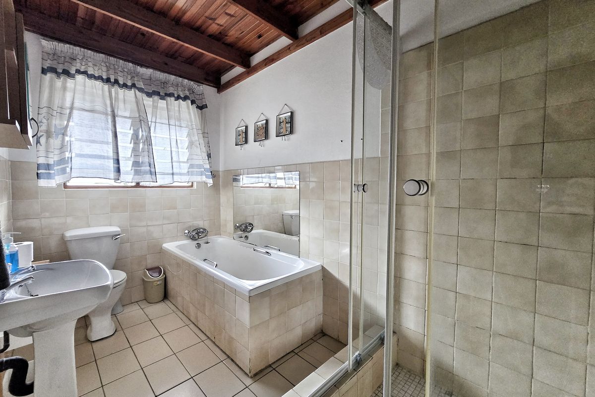 A functional bathroom featuring a pedestal basin, toilet, built-in bathtub, and a separate shower enclosure with tiled finishes and exposed timber ceiling beams.