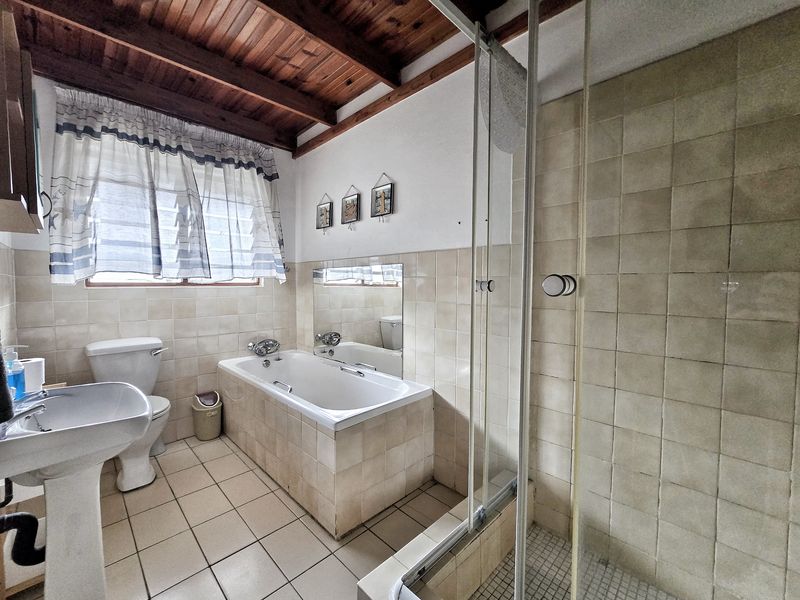 A functional bathroom featuring a pedestal basin, toilet, built-in bathtub, and a separate shower enclosure with tiled finishes and exposed timber ceiling beams.