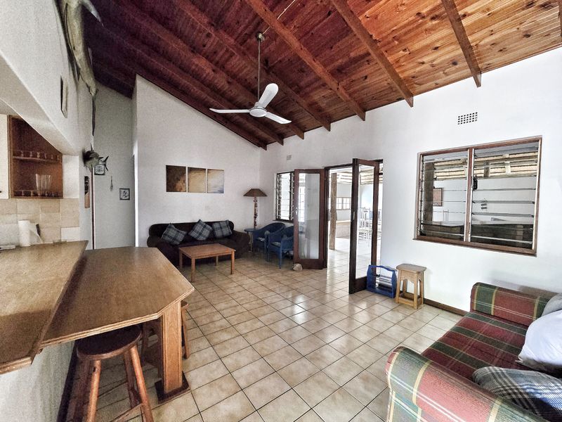 Spacious open-plan living area featuring a high exposed timber rafter ceiling, ceramic tiled flooring, and a breakfast bar connecting to the kitchen space.